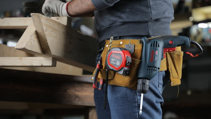 A woodworker with a belt with a corded drill attached